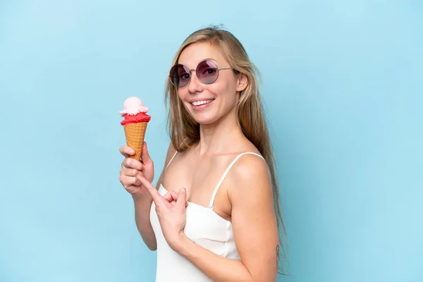 青い背景に隔離されたアイスクリームを保持し それを指す水着の若い金髪の女性 — ストック写真