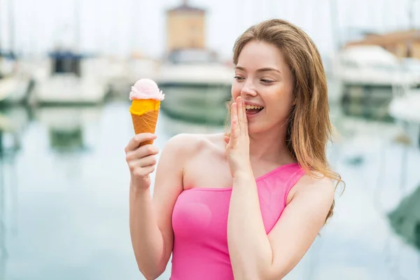 Young redhead woman with a cornet ice cream at outdoors with surprise and shocked facial expression