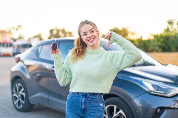 Young pretty girl holding car keys at outdoors proud and self-satisfied