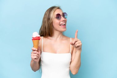 Mavi arka planda izole edilmiş bir dondurma tutan mayo giymiş genç sarışın kadın çözümü bulmak için parmağını kaldırıyor.