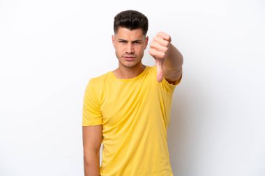Beyaz arka planda izole genç beyaz adam olumsuz ifade ile baş parmağını göstermektedir