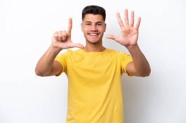 Beyaz arka planda izole edilmiş genç beyaz adam yediyi parmaklarıyla sayıyor