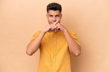 Young caucasian man isolated on beige background showing a sign of silence gesture