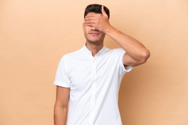 Young caucasian man isolated on beige background covering eyes by hands. Do not want to see something