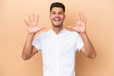 Beyazlı genç bir adam bej arka planda izole edilmiş. Parmaklarıyla ona kadar sayıyor.