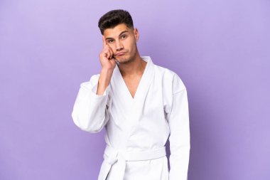 Mor arka planda karate yapan genç beyaz bir adam bir fikir düşünüyor.