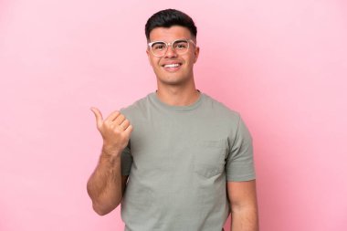 Pembe arka planda izole edilmiş beyaz, yakışıklı genç bir adam bir ürün sunmak için kenarı işaret ediyor.