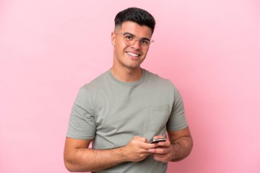 Pembe arka planda izole edilmiş genç beyaz adam cep telefonuyla bir mesaj gönderiyor.