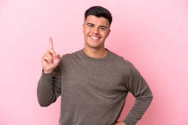 Pembe arka planda izole edilmiş beyaz, yakışıklı genç bir adam en iyinin işareti olarak parmağını kaldırıyor.