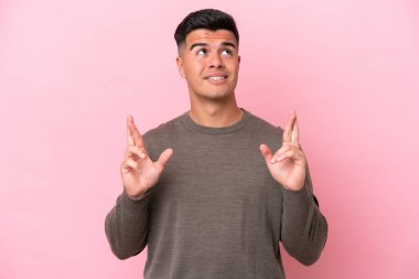 Beyaz tenli yakışıklı adam pembe arka planda izole edilmiş, parmaklarını çapraz yapıp en iyisini diliyor.