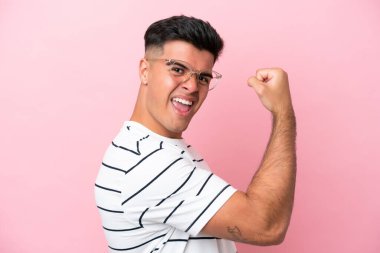 Pembe arka planda, gözlüklü ve zaferi kutlayan beyaz tenli yakışıklı bir adam.