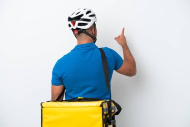 Beyaz arka planda izole edilmiş termal sırt çantalı beyaz bir adam işaret parmağıyla işaret ediyor.