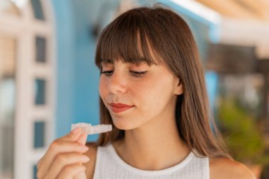 Dışarıdaki genç kadın görünmez diş telleri tutuyor.