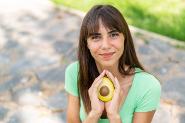 Dışarıda elinde avokado tutan genç bir kadın.