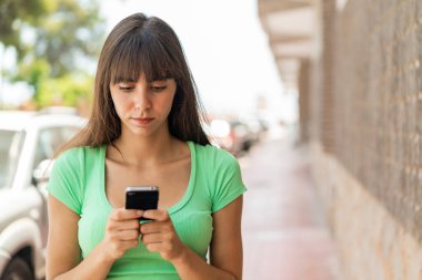 Açık havada cep telefonu kullanan genç bir kadın.