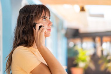 Dışarıda genç bir kadın cep telefonuyla birileriyle sohbet ediyor.