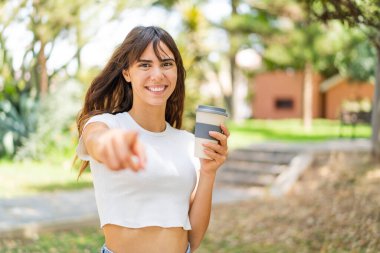Açık havada kahve içen genç bir kadın kendinden emin bir ifadeyle seni işaret ediyor.