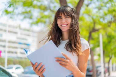 Dışarıda elinde bir defter tutan genç bir kadın.