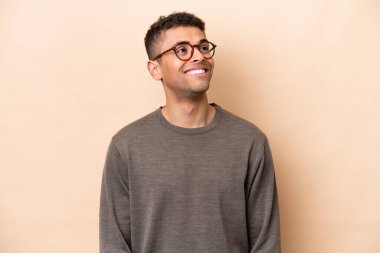 Young Brazilian man isolated on beige background thinking an idea while looking up