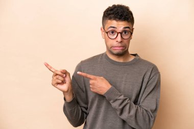 Bej arka planda izole edilmiş genç Brezilyalı adam korkmuş ve kenarı işaret ediyor.