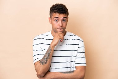 Young Brazilian man isolated on beige background having doubts and thinking