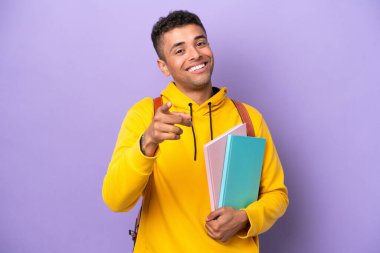 Mor arka planda izole edilmiş Brezilyalı genç bir adam mutlu bir ifadeyle öne işaret ediyor.