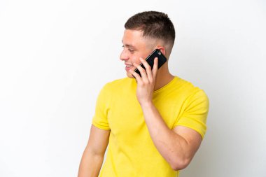 Beyaz arka planda izole edilmiş genç Brezilyalı bir adam cep telefonuyla sohbet ediyor.