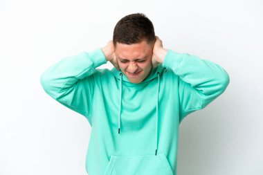 Beyaz arka planda izole edilmiş genç Brezilyalı adam hayal kırıklığına uğramış ve kulaklarını kapatmış.