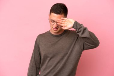 Genç Brezilyalı adam pembe arka planda izole edilmiş, yorgun ve hasta bir ifadeyle.
