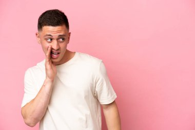 Pembe arka planda izole edilmiş genç Brezilyalı adam yan tarafa bakarken sürpriz bir jest yapıyor.