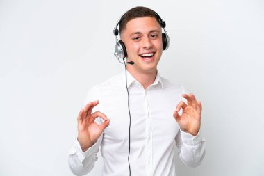 Telemarketer Brazilian man working with a headset isolated on white background showing an ok sign with fingers