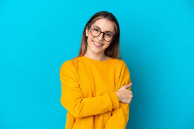 Mavi arka planda izole edilmiş genç beyaz kadın gülüyor.