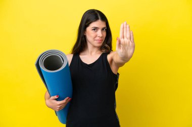 İtalyan spor kadını yoga derslerine gidiyor. Sarı arka planda izole bir şekilde. Durma hareketi yapıyor.