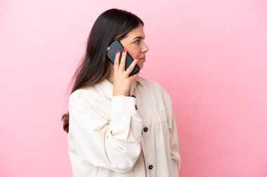 Pembe arka planda izole edilmiş genç bir İtalyan kadın cep telefonuyla biriyle sohbet ediyor.