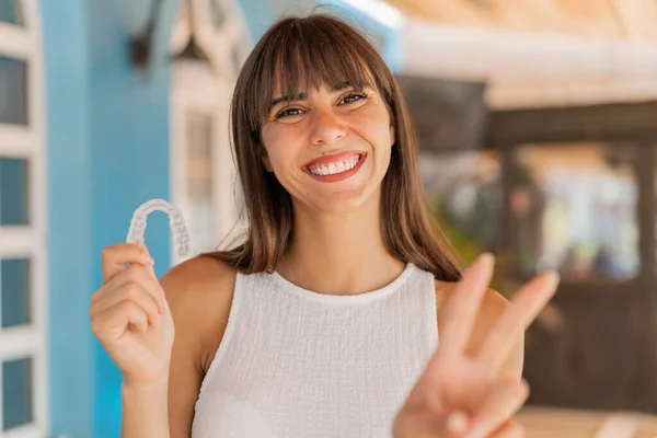 Young woman holding invisible braces at outdoors smiling and showing victory sign