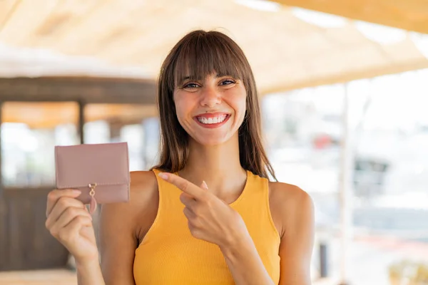 屋外で財布を持ち それを指差している若い女性 — ストック写真