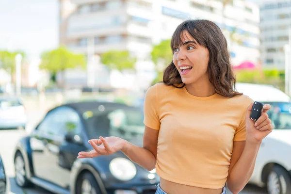 驚きの表情で屋外で車の鍵を握っている若い女性 — ストック写真