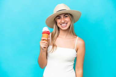 Young caucasian woman in swimsuit with a cornet ice cream isolated on blue background smiling a lot