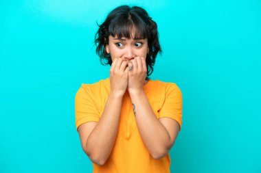 Arjantinli genç bir kadın mavi arka planda izole edilmiş gergin ve korkmuş bir şekilde elleriyle suni teneffüs yapıyor.