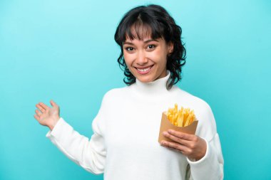 Arjantinli genç bir kadın elinde kızarmış cipslerle mavi arka planda izole bir şekilde elini uzatıyor.