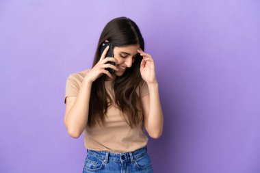 Mor arka planda izole edilmiş cep telefonu kullanan beyaz bir kadın.