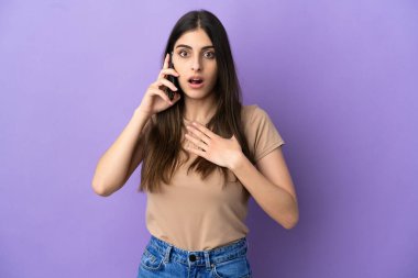 Mor arka planda izole edilmiş cep telefonu kullanan beyaz bir kadın sağa bakarken şaşırmış ve şok olmuştu.