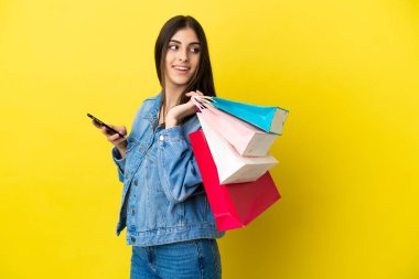 Mavi arka planda izole edilmiş beyaz bir kadın. Elinde alışveriş çantaları ve cep telefonu var.
