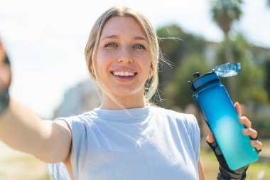 Açık havada bir şişe suyla spor yapan genç sarışın kadın.