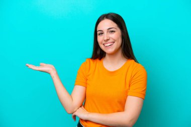 Mavi arka planda izole edilmiş genç beyaz kadın bir ilan vermek için avucunun içinde hayali bir fotokopi makinesi tutuyor.