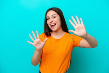 Mavi arka planda izole edilmiş genç beyaz kadın parmaklarıyla ona kadar sayıyor.