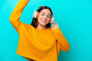 Genç kız mavi arka planda izole edilmiş müzik ve dans dinliyor.
