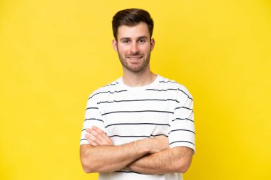 Sarı arka planda izole genç beyaz adam kollarını ön cephede çapraz tutuyor.