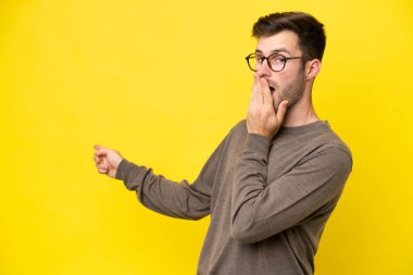 Sarı arka planda izole edilmiş genç beyaz bir adam sürpriz bir ifadeyle işaret ederken...