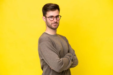 Sarı arka planda izole edilmiş, kolları çapraz ve ileriye bakan genç beyaz bir adam.